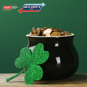 A large glittery shamrock leaning against a pot of gold sitting on top of a wooden table.